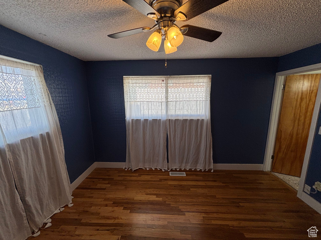 Empty room with a textured ceiling, a ceiling fan, baseboards, and wood finished floors