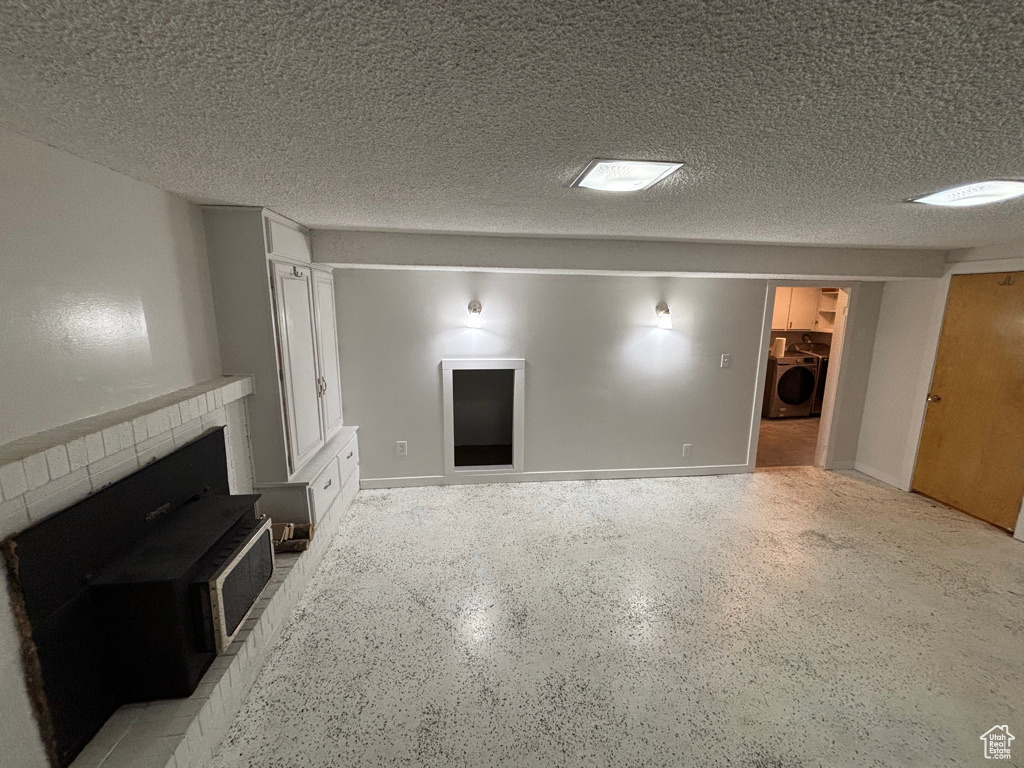Unfurnished living room featuring baseboards, a textured ceiling, washer / dryer, and a fireplace