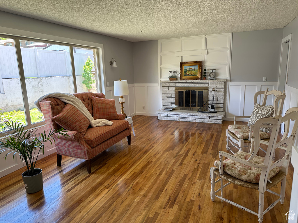 Living room featuring wood finished floors, a decorative wall, wainscoting, a stone fireplace, and a textured ceiling
