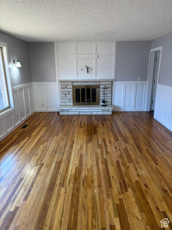 Unfurnished living room with hardwood / wood-style floors, visible vents, a fireplace, a textured ceiling, and a decorative wall