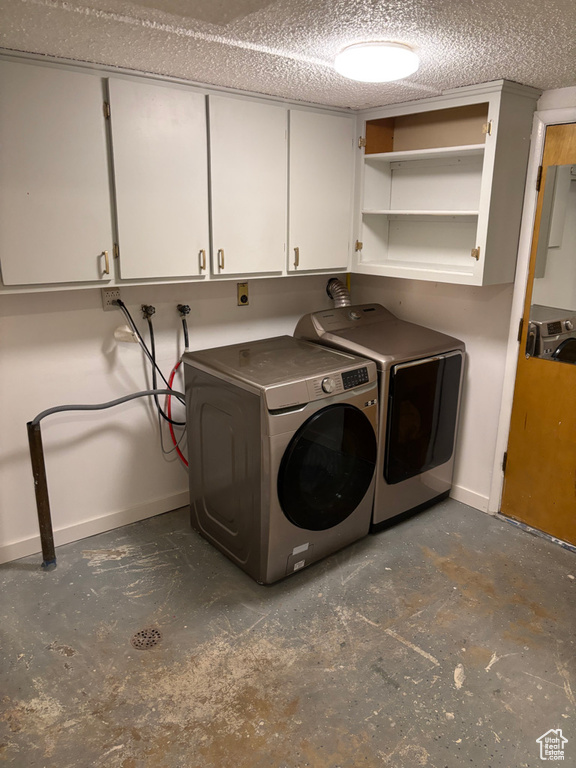 Washroom featuring washing machine and clothes dryer, cabinet space, a textured ceiling, and baseboards