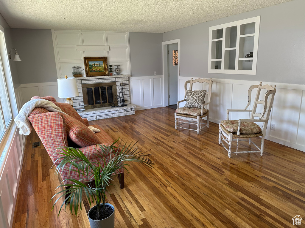 Living area with a textured ceiling, wood finished floors, a wainscoted wall, a decorative wall, and a stone fireplace