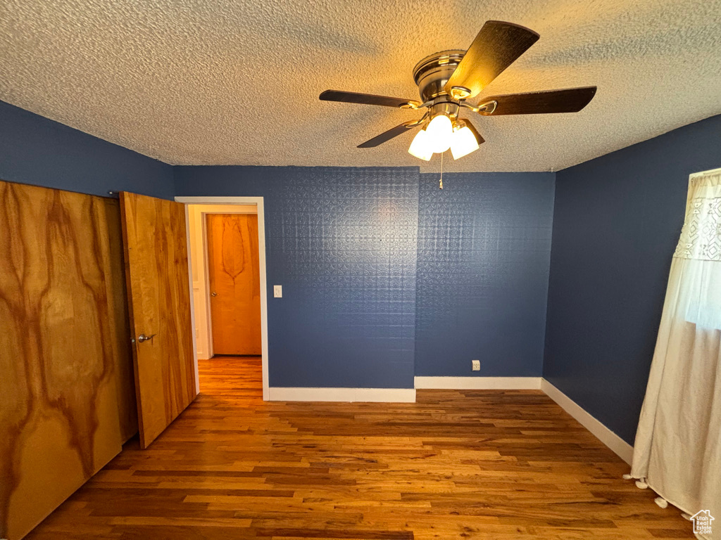 Empty room with baseboards, a textured ceiling, ceiling fan, and wood finished floors