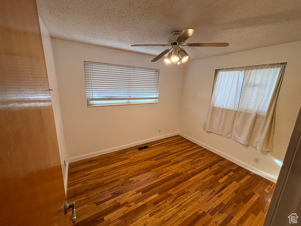 Empty room with wood finished floors, visible vents, and baseboards