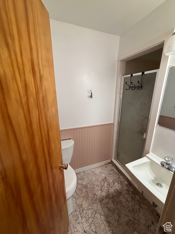 Full bathroom featuring a wainscoted wall, toilet, marble finish floor, a stall shower, and a sink