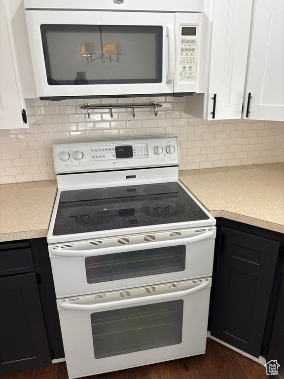 Kitchen featuring white appliances, light countertops, dark wood-type flooring, white cabinetry, and tasteful backsplash