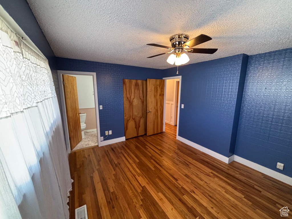 Unfurnished bedroom featuring visible vents, connected bathroom, baseboards, wood finished floors, and a textured ceiling
