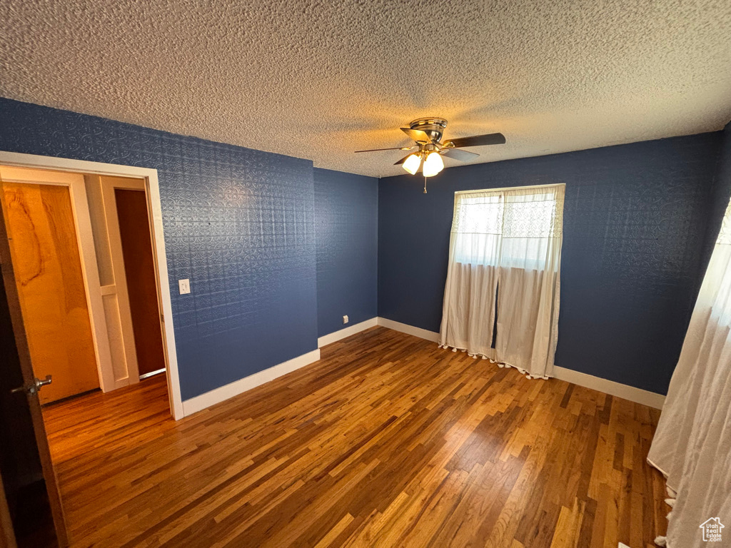 Unfurnished bedroom featuring a textured ceiling, a ceiling fan, baseboards, and wood finished floors