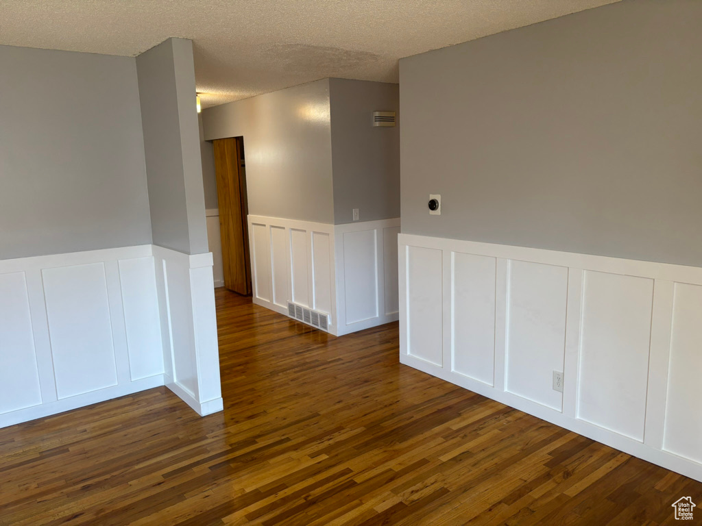 Empty room with visible vents, wainscoting, dark wood-style floors, a decorative wall, and a textured ceiling