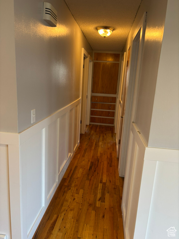 Corridor with dark wood-type flooring, a decorative wall, a wainscoted wall, and a textured ceiling