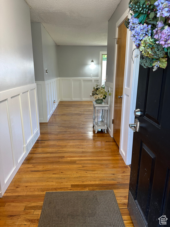 Corridor featuring a decorative wall, a wainscoted wall, wood finished floors, and a textured ceiling