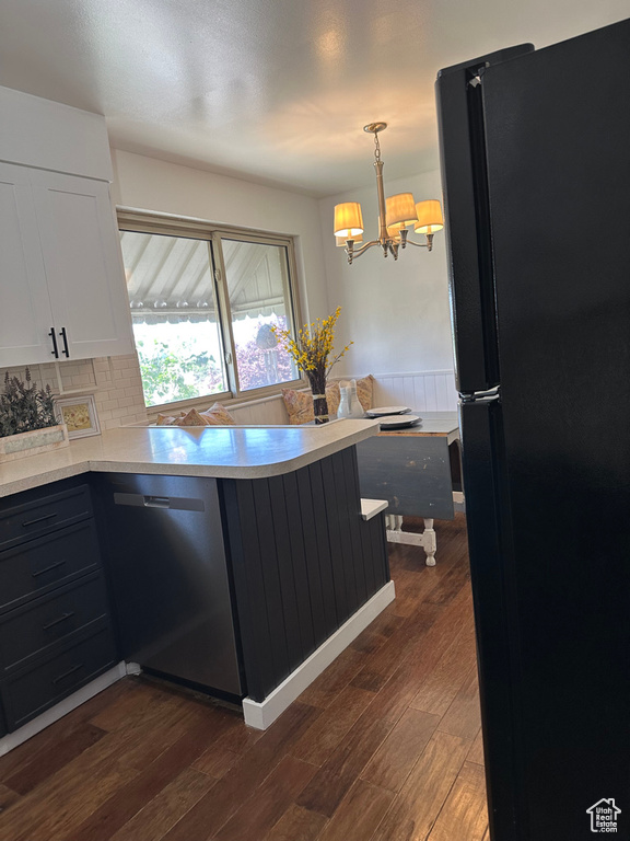 Kitchen featuring freestanding refrigerator, stainless steel dishwasher, white cabinetry, dark wood-style floors, and a peninsula
