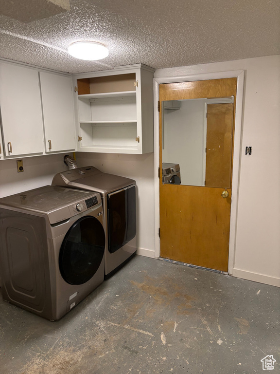 Clothes washing area with cabinet space, washing machine and dryer, a textured ceiling, and baseboards