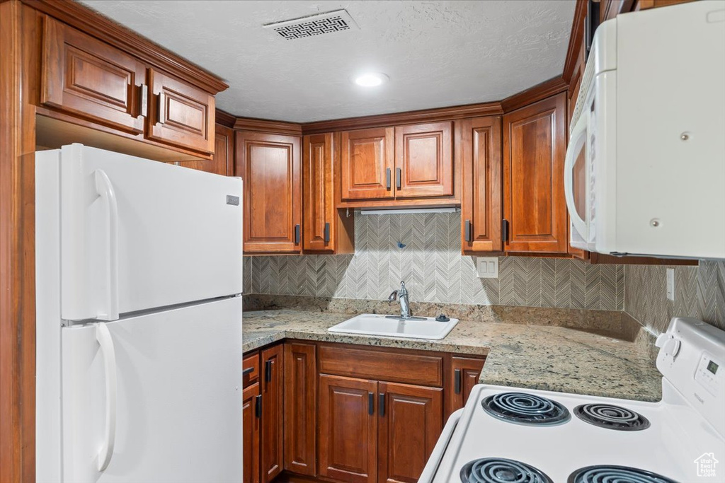 Kitchen with white appliances, brown cabinetry, visible vents, a sink, and tasteful backsplash