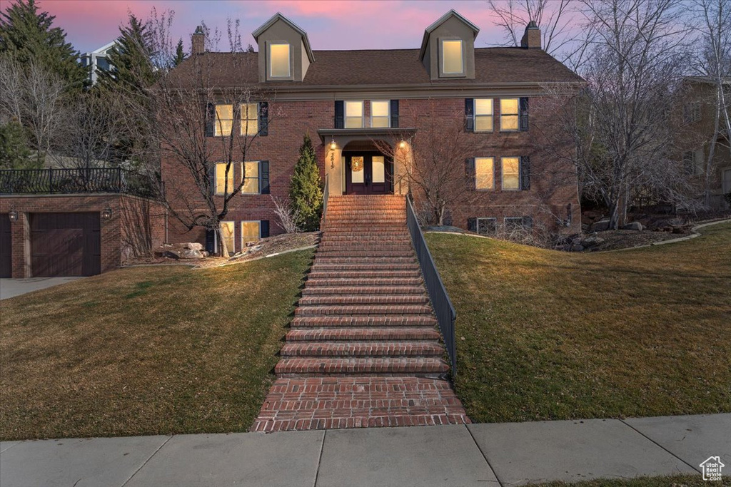 View of front of house with stairway, a front yard, a garage, brick siding, and a chimney