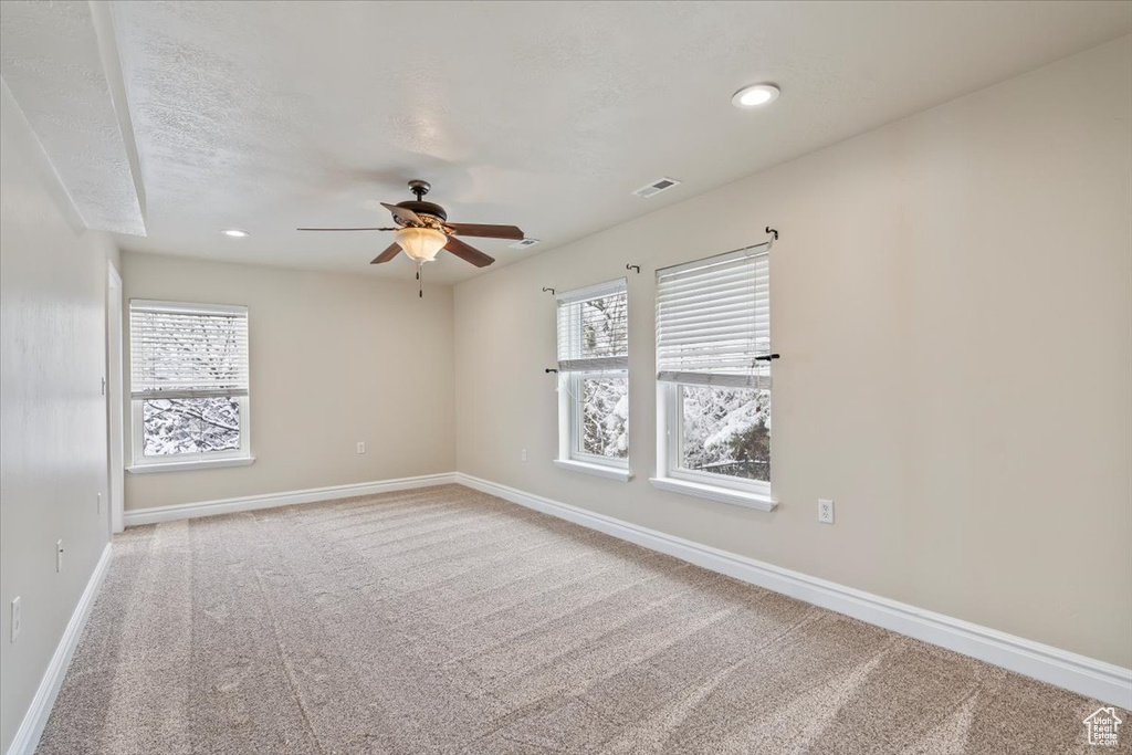 Empty room with a wealth of natural light, ceiling fan, baseboards, and carpet floors