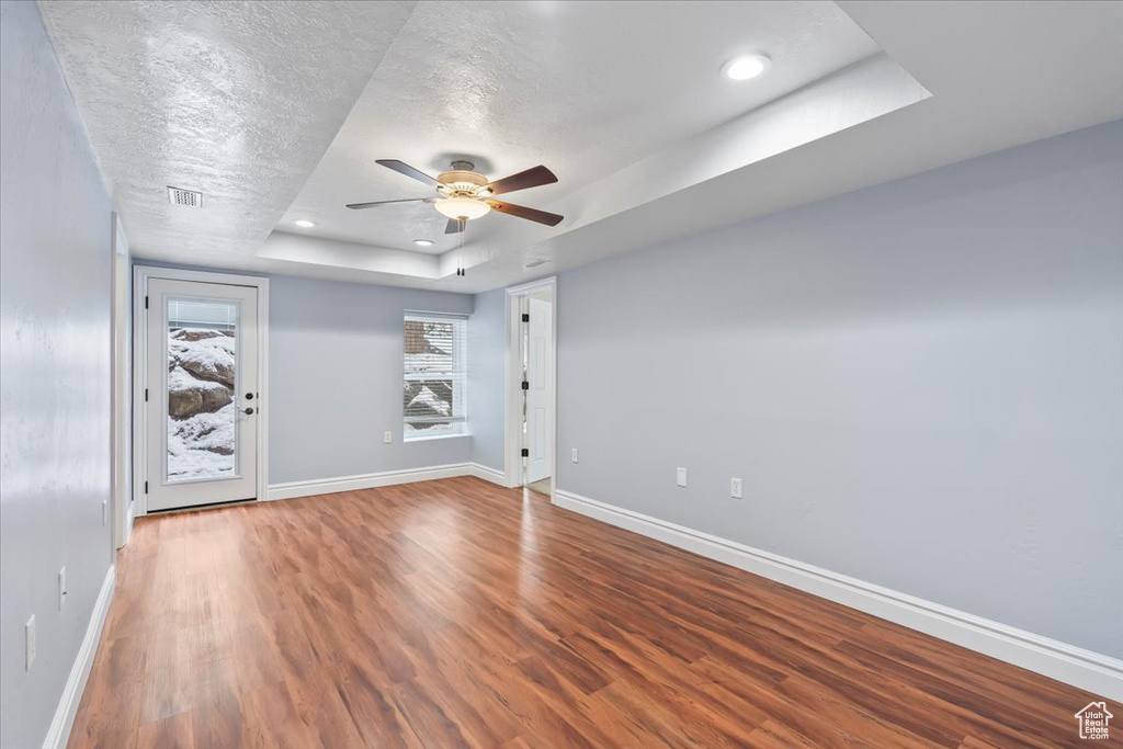 Spare room featuring a raised ceiling, a ceiling fan, a textured ceiling, wood finished floors, and baseboards