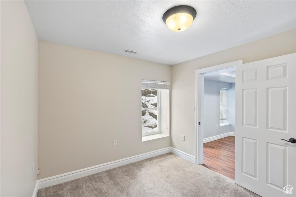 Empty room featuring a textured ceiling, carpet, visible vents, and baseboards
