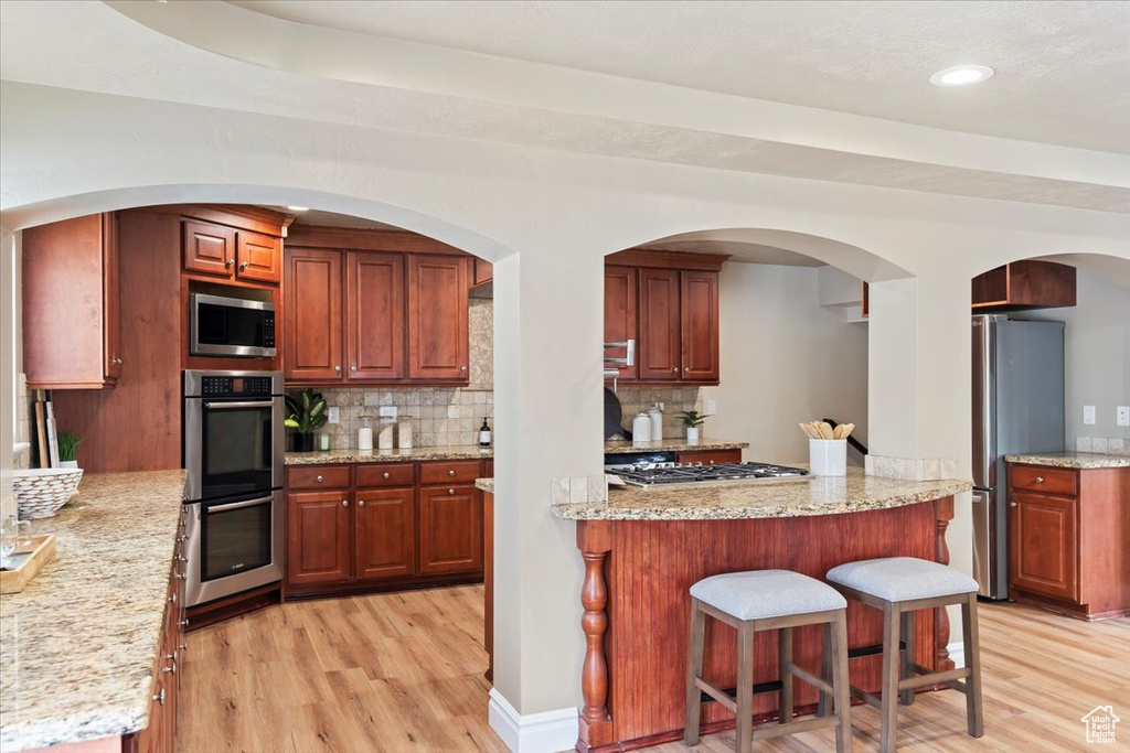 Kitchen featuring a breakfast bar, light wood-style floors, tasteful backsplash, and appliances with stainless steel finishes