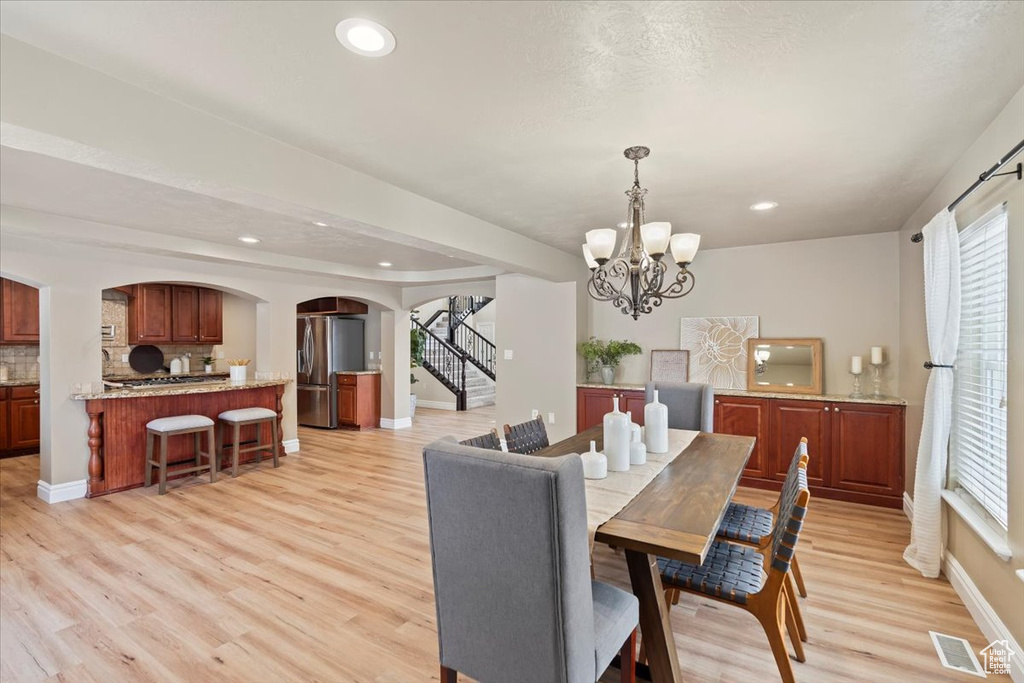 Dining area with light wood finished floors, visible vents, a chandelier, stairs, and arched walkways