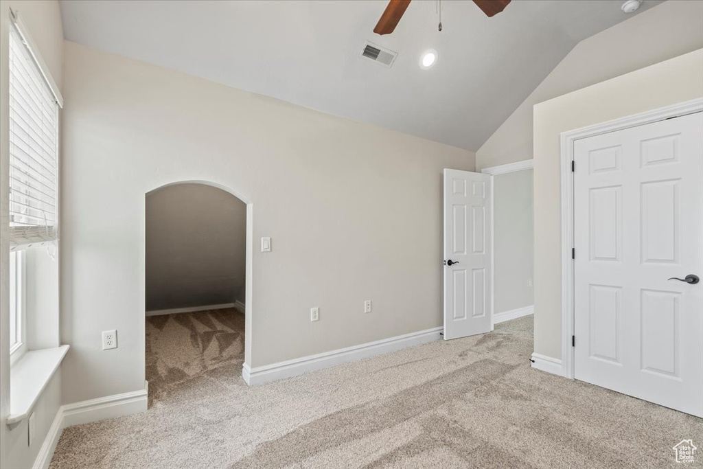 Unfurnished bedroom with visible vents, baseboards, lofted ceiling, carpet floors, and arched walkways