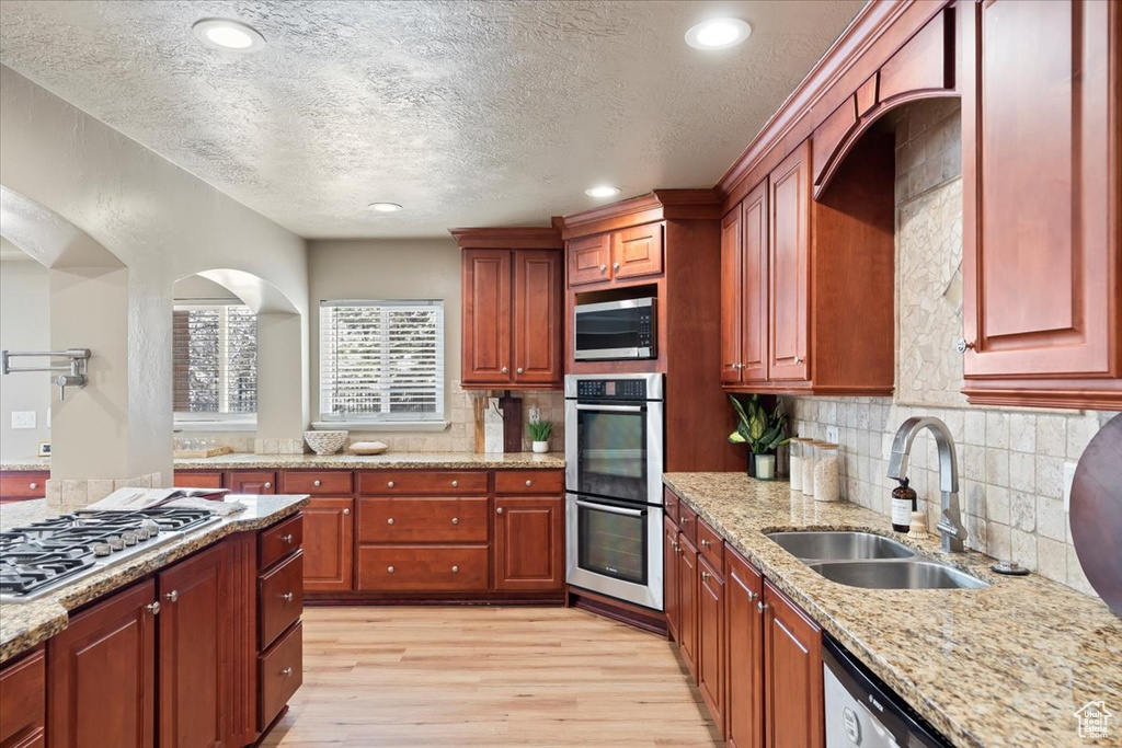 Kitchen with light stone countertops, light wood-style flooring, a sink, appliances with stainless steel finishes, and backsplash