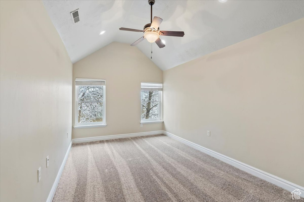 Carpeted empty room featuring visible vents, a ceiling fan, baseboards, and vaulted ceiling