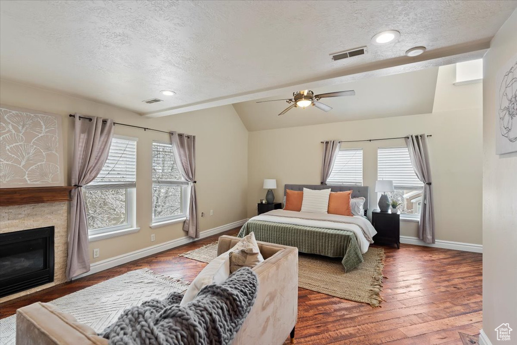 Bedroom with visible vents, multiple windows, a stone fireplace, and vaulted ceiling
