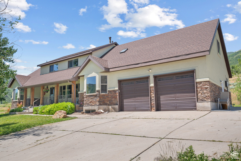 View of front facade with stucco siding, stone siding, driveway, and a porch