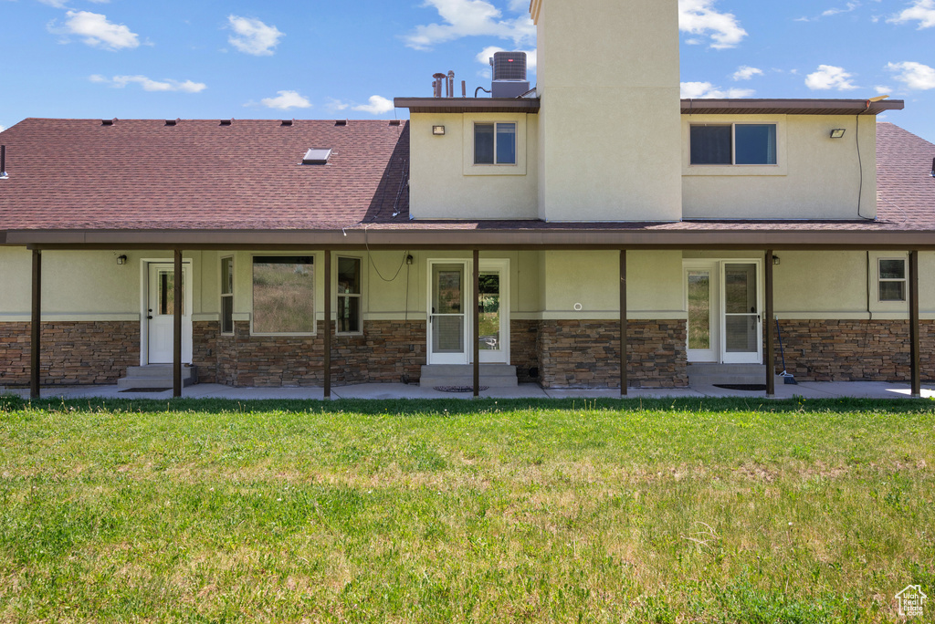 Rear view of property featuring stone siding, entry steps, stucco siding, a yard, and a chimney