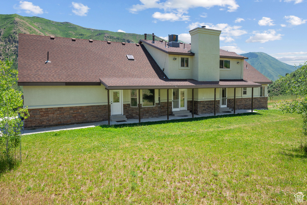 Rear view of house with a mountain view, stone siding, a lawn, and stucco siding