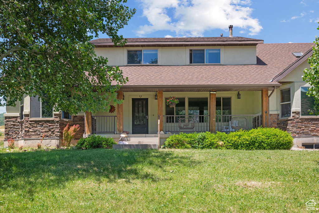Townhome / multi-family property featuring stucco siding, stone siding, covered porch, a front lawn, and roof with shingles