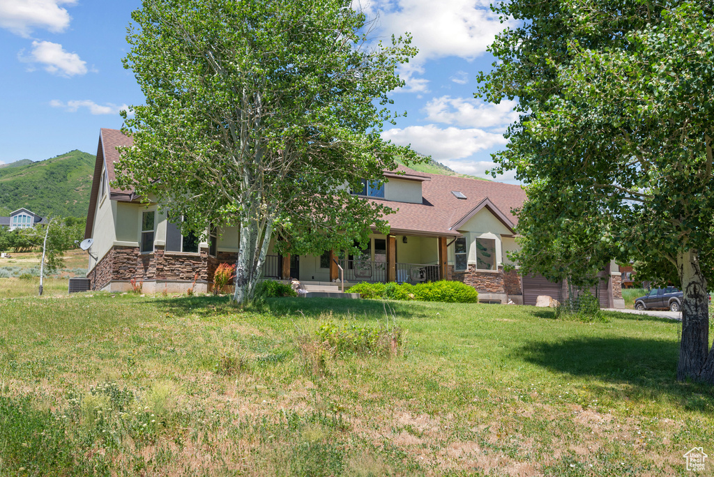 Obstructed view of property with stone siding, covered porch, a front yard, a mountain view, and stucco siding
