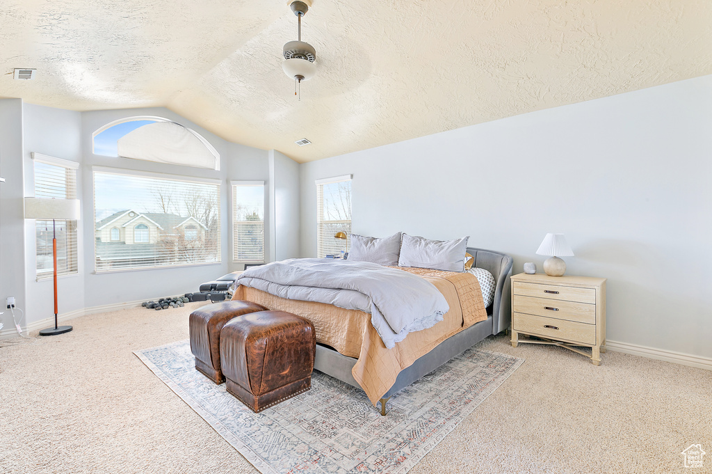 Carpeted bedroom with a ceiling fan, visible vents, baseboards, lofted ceiling, and a textured ceiling