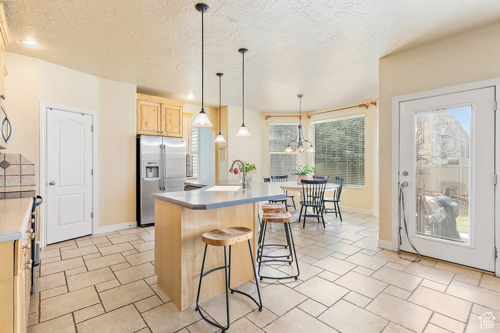 Kitchen featuring a kitchen island, a sink, light brown cabinetry, stainless steel appliances, and a kitchen bar