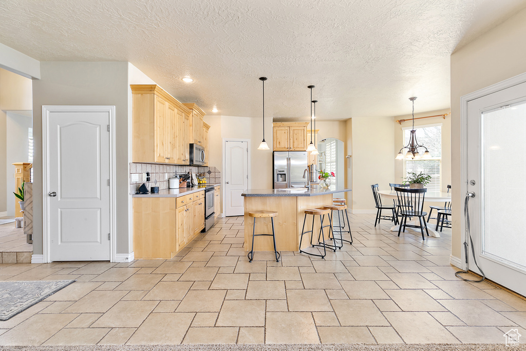 Kitchen with decorative backsplash, light brown cabinets, stainless steel appliances, and a kitchen bar