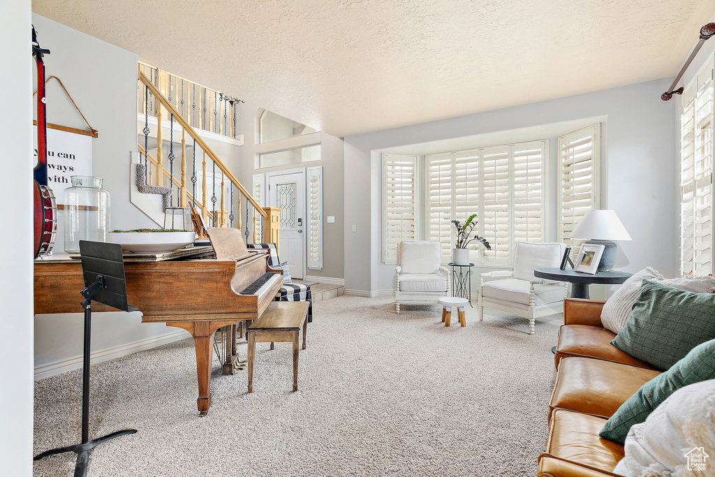 Carpeted living room featuring a textured ceiling, stairs, and baseboards