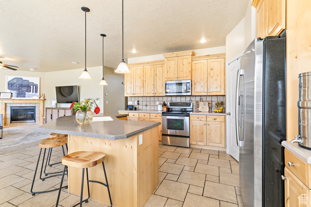 Kitchen with light brown cabinets, open floor plan, backsplash, and stainless steel appliances