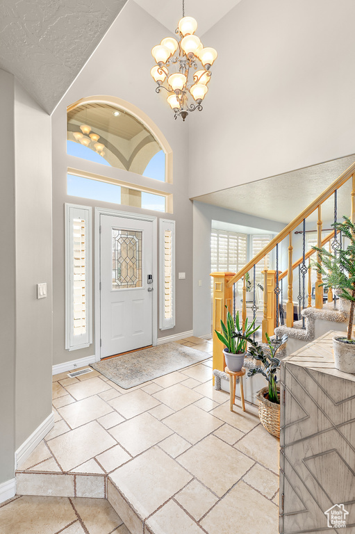 Foyer with stone tile flooring, an inviting chandelier, baseboards, a towering ceiling, and stairs