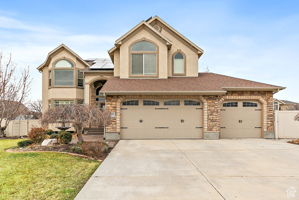 View of front of home with roof mounted solar panels, fence, driveway, and stucco siding