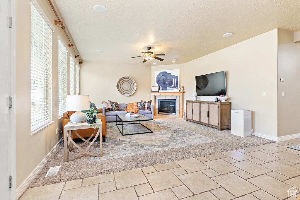 Living room with visible vents, a textured ceiling, baseboards, ceiling fan, and a tile fireplace