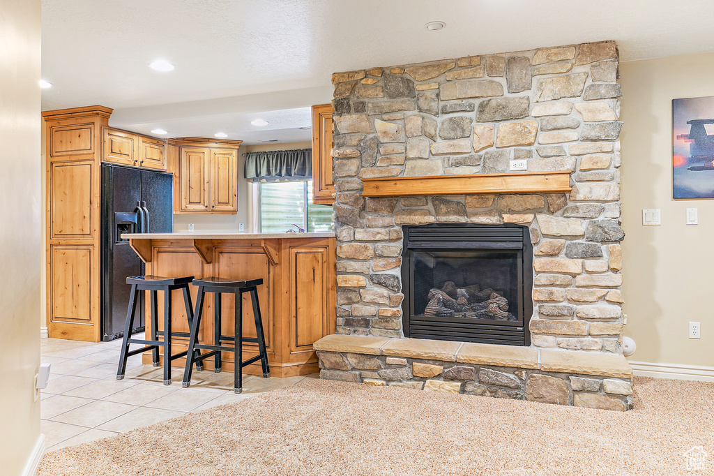 Kitchen featuring baseboards, a kitchen bar, light tile patterned floors, a stone fireplace, and black fridge