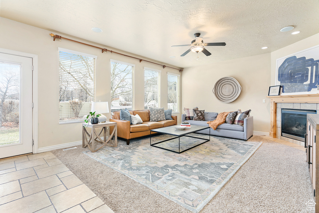 Living area featuring baseboards, visible vents, ceiling fan, a tile fireplace, and a textured ceiling