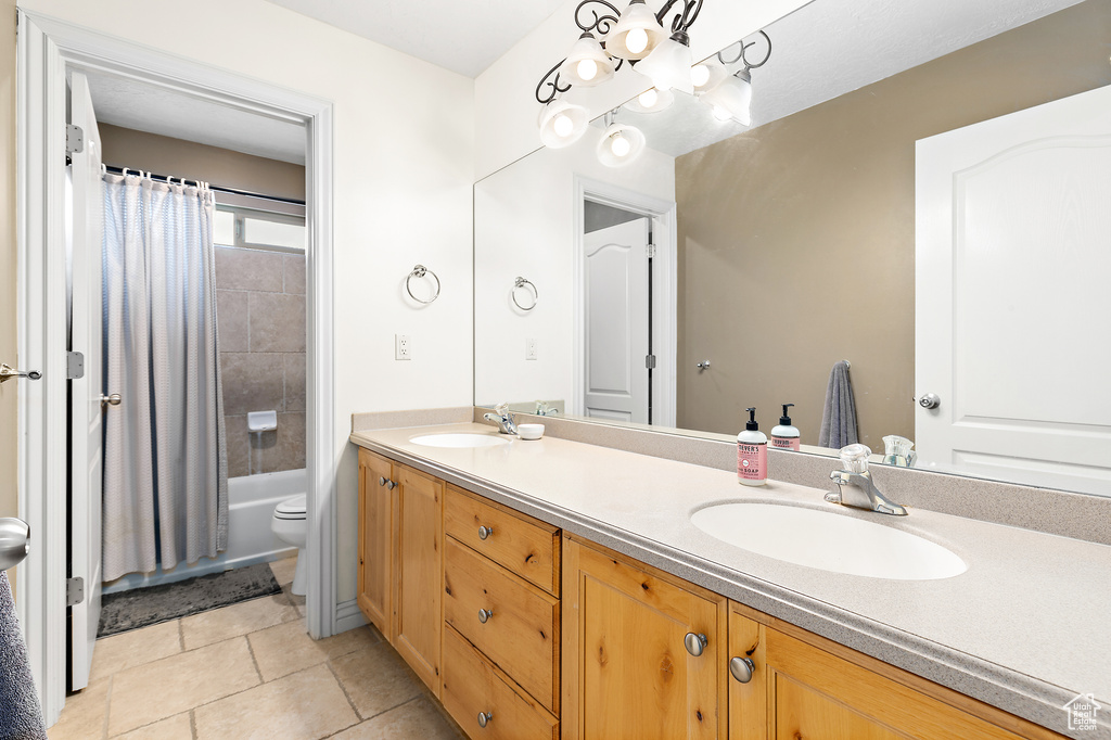 Full bathroom featuring double vanity, tile patterned floors, toilet, and a sink