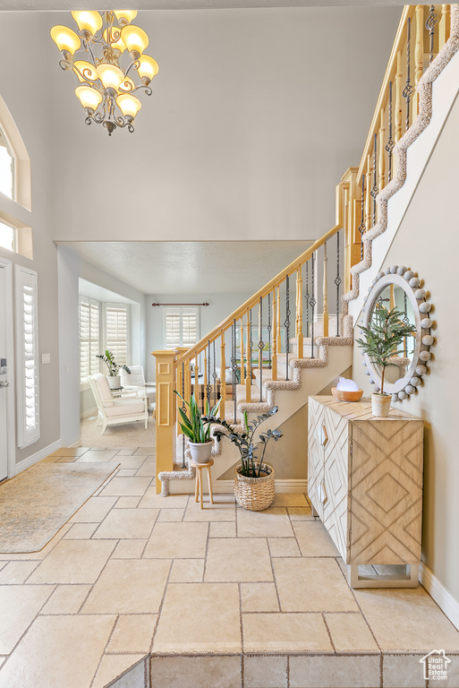 Entryway featuring a notable chandelier, stone tile flooring, a high ceiling, baseboards, and stairs