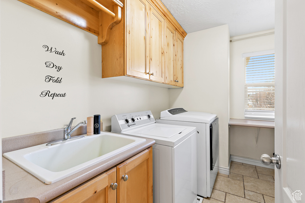 Laundry room with a sink, stone tile floors, cabinet space, separate washer and dryer, and baseboards