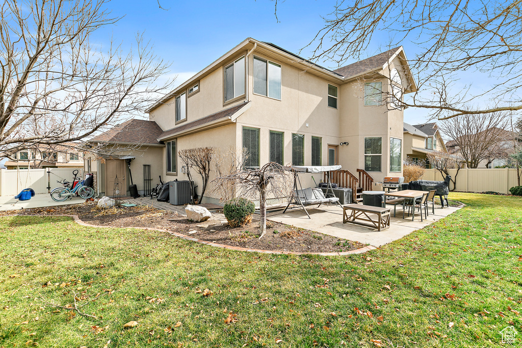 Rear view of house featuring fence, central AC unit, stucco siding, a yard, and a patio