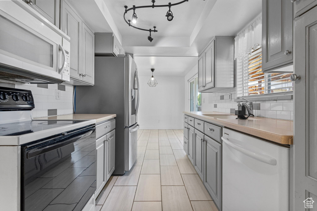 Kitchen featuring white appliances, a sink, gray cabinetry, light countertops, and tasteful backsplash