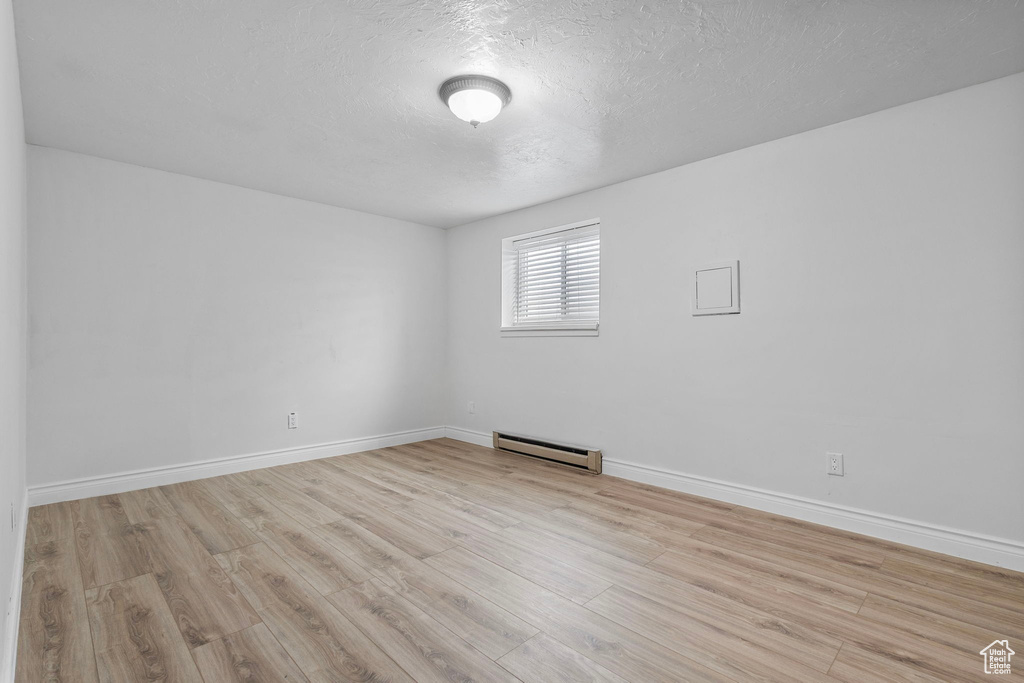 Unfurnished room with a baseboard radiator, baseboards, a textured ceiling, and wood finished floors