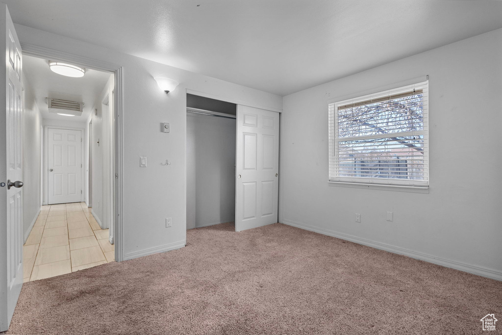 Unfurnished bedroom featuring visible vents, baseboards, light tile patterned flooring, a closet, and light carpet